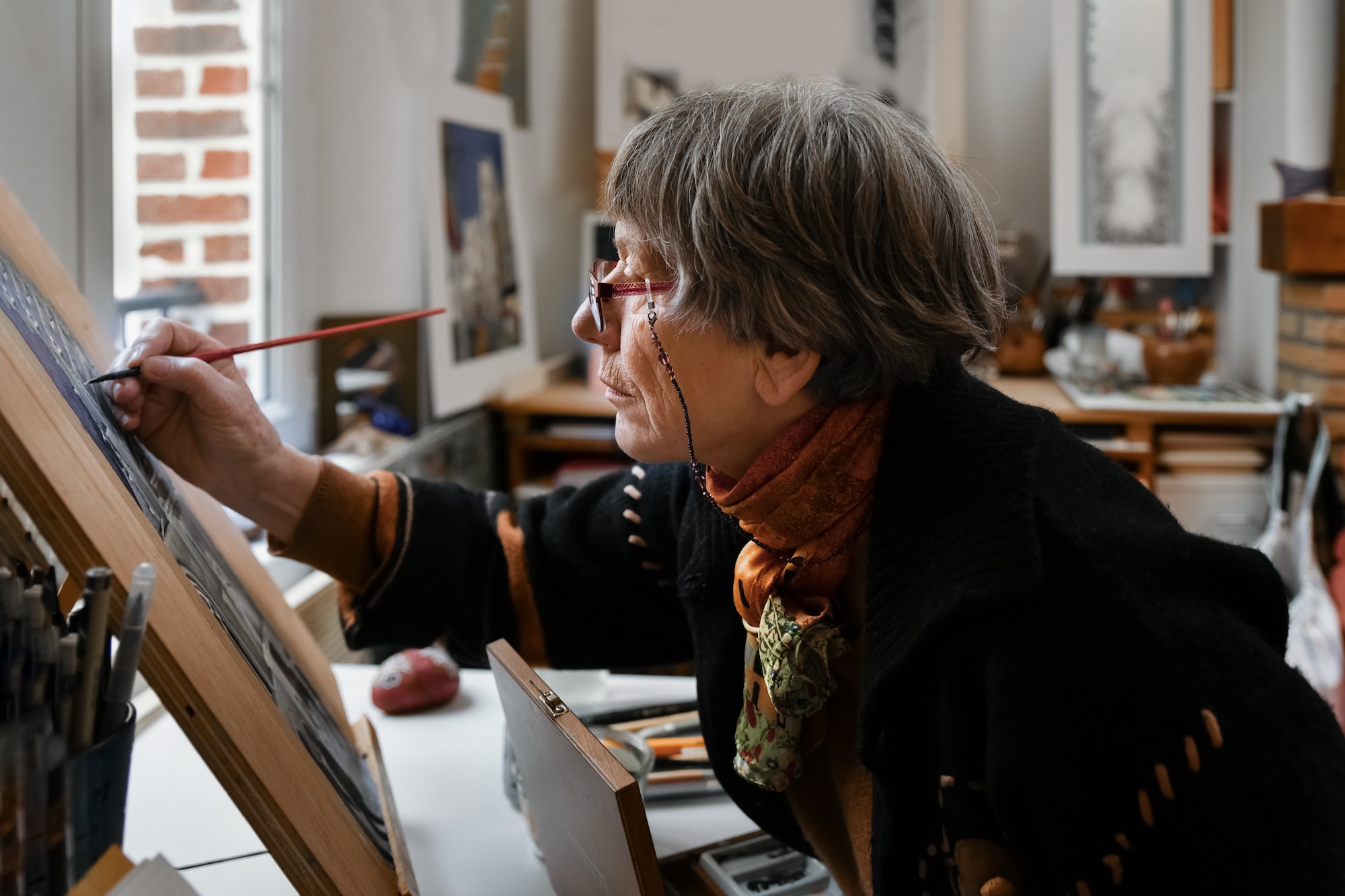 An old woman artist paints a picture at home